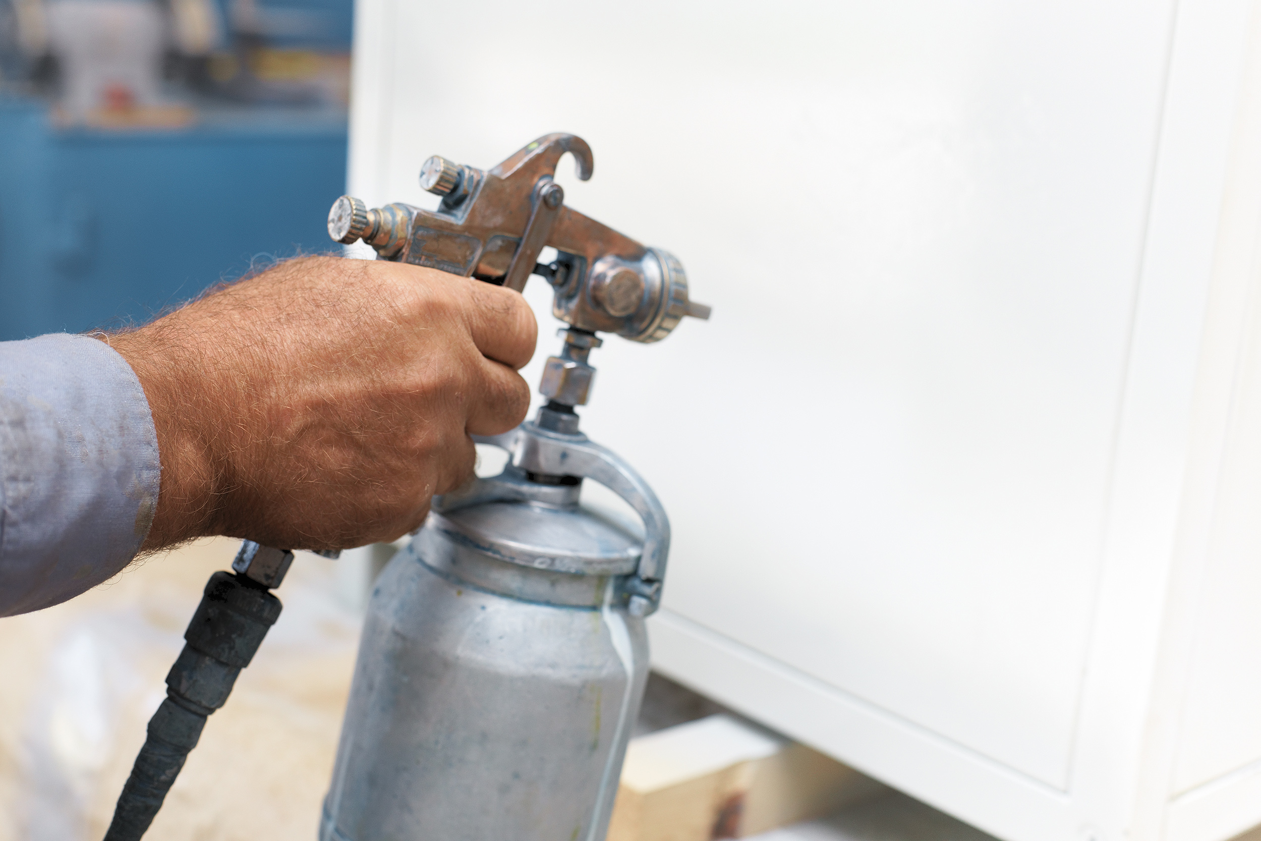 Painting of a metal product. A workshop worker holds a compressor spray gun in his hand and paints the Cabinet white. The hand with the tool close up